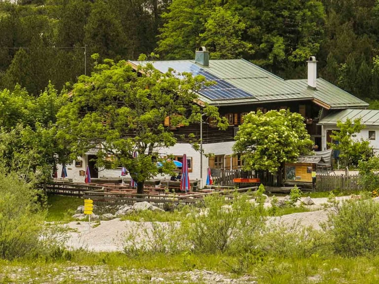 Blick auf die Wimbachgrieshütte mit grünem Blechdach und Terrasse, umgeben von dichtem Bergwald.