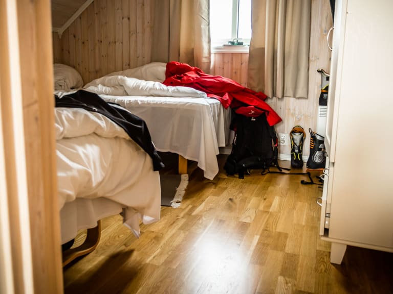 Zwei Einzelbetten im Schlafzimmer der Svinoya Rorbuer mit heller Holzverkleidung und Bergausrüstung am Boden.