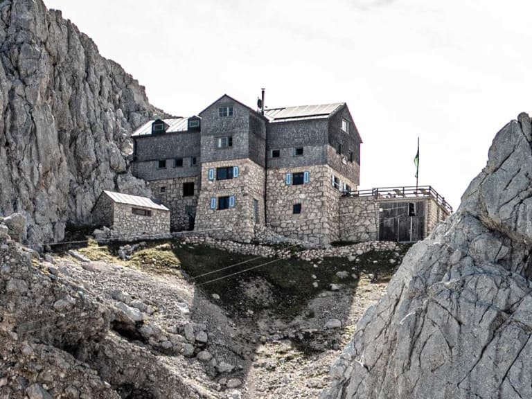 Die Meilerhütte aus hellem Naturstein steht in exponierter Lage zwischen schroffen Felswänden im Wettersteingebirge.