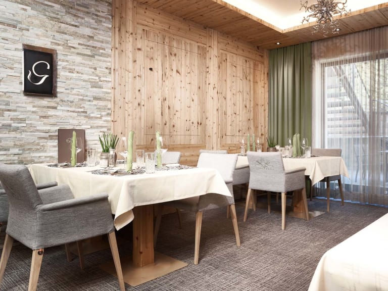 Speisesaal im Hotel Gundolf mit Natursteinwand, gedeckten Tischen und alpinem Design.