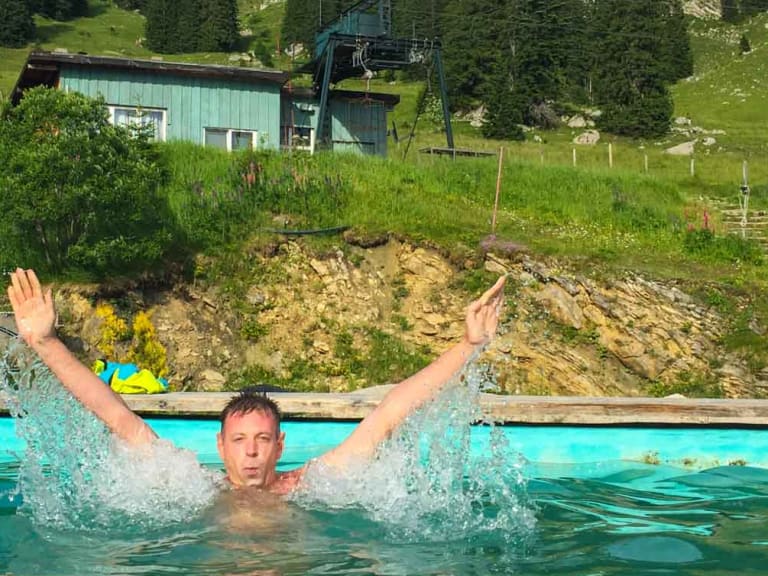 Badegast im Schwimmbecken mit Blick auf die Obere Maxlraineralm und Bergpanorama im Hintergrund.