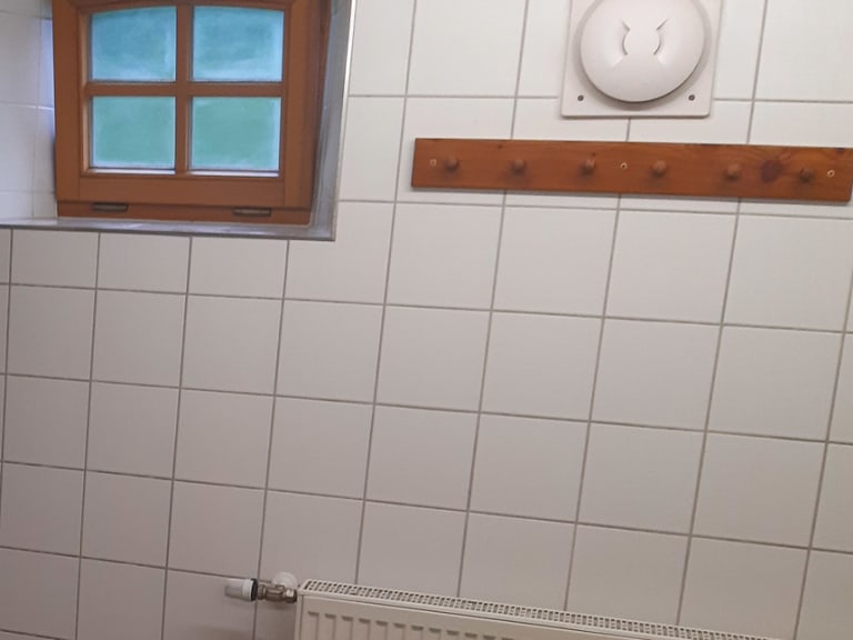 Gefliester Duschbereich in der Albert-Link-Hütte mit offener Dusche und Heizung unter kleinem Fenster.