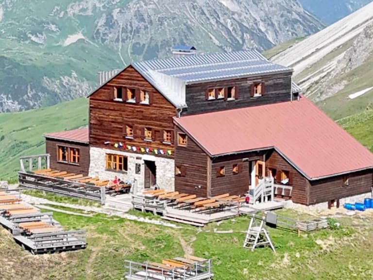 Panoramablick auf die Stuttgarter Hütte mit traditioneller Holzbauweise vor schneebedeckten Gipfeln der Lechtaler Alpen.
