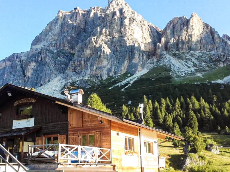 Das Rifugio Col Gallina mit großer Terrasse und weißen Sonnenschirmen vor hohen Kalksteinwänden.