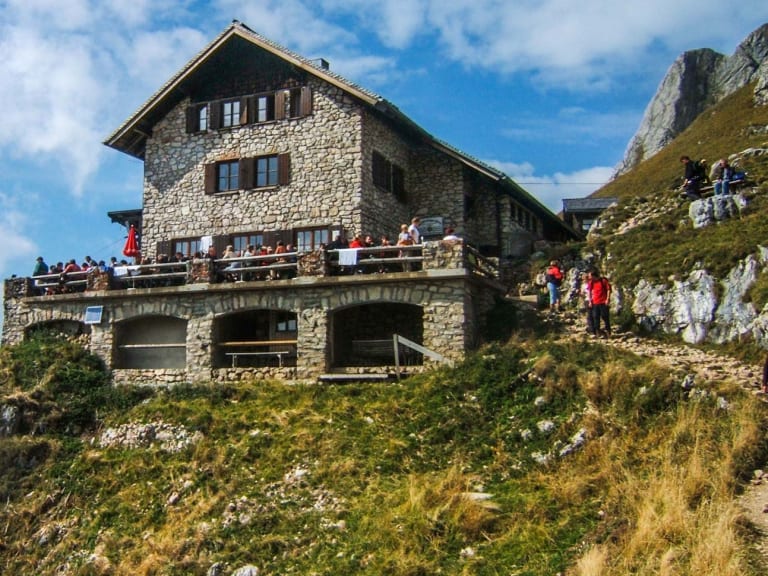 Wanderer versammeln sich auf der Terrasse der Bad Kissinger Hütte am steilen Berghang mit Blick ins Tal.