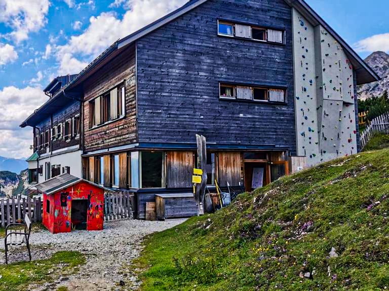 Das Solsteinhaus zeigt sich als traditionelle Holzhütte mit modernem Anbau auf einer Almwiese im Karwendel.