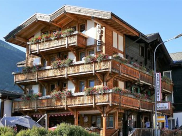 Hotel Grimsel mit mehrstöckiger Holzfassade und Hotelschild an der Gebäudeecke in alpiner Umgebung.