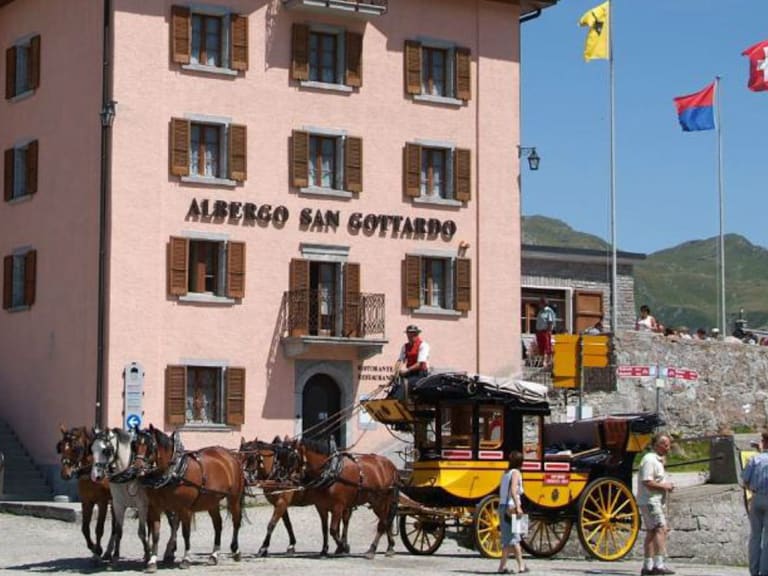 Das rosa Albergo San Gottardo am Gotthardpass mit einer historischen Postkutsche vor dem Haupteingang.
