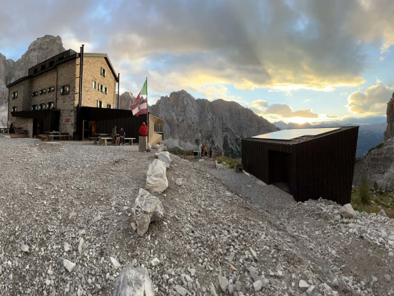 Bergwanderer vor dem Rifugio Brentei auf einem Schuttplateau in den Dolomiten bei bewölktem Himmel.