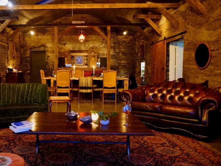 Rustikaler Gastraum der Holy Ram Lodge mit Natursteinwänden, Chesterfield-Sofas und Kamin für gemütliche Abende.