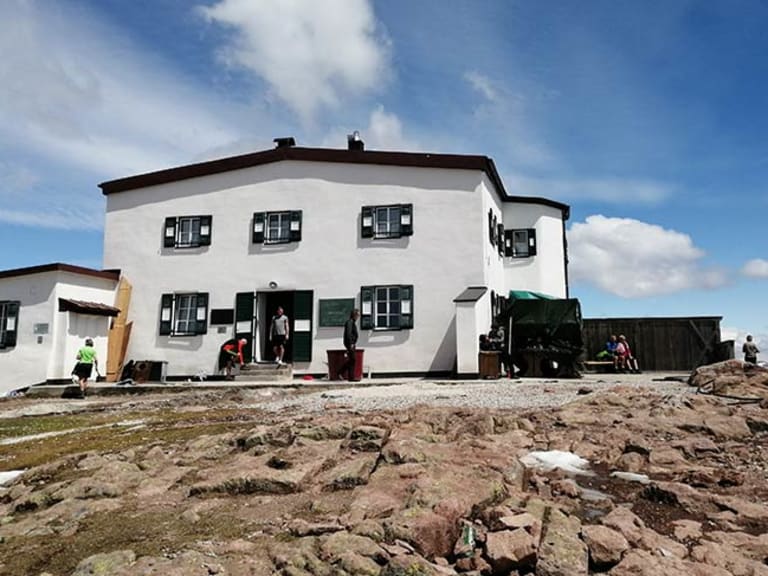 Das Schutzhaus Rittner Horn steht auf felsigem Bergplateau mit Besuchern auf der Terrasse.