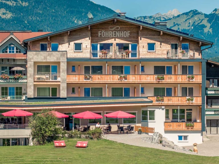Außenansicht des Hotel Föhrenhof mit roter Sonnenterrasse und Blick auf die Lechtaler Alpen.