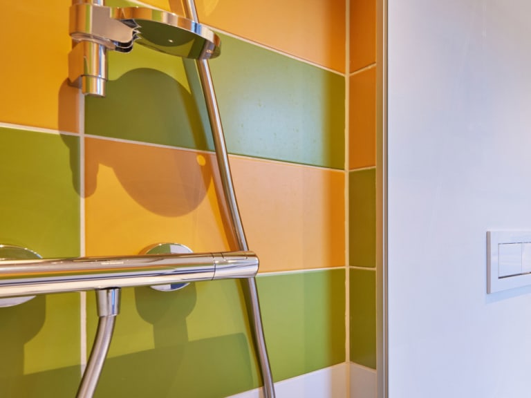 Badezimmer im Explorer Hotel Stubaital mit farbiger Wandgestaltung und Glasdusche.