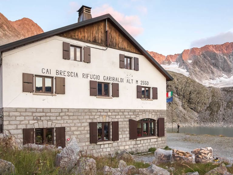 Das Rifugio Giuseppe Garibaldi steht auf 2.550 m Höhe vor einer verschneiten Felswand in der Adamello-Gruppe.