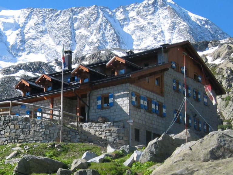 Das Rifugio Stavèl Denza auf 2.298 m mit schneebedeckter Presanella und Gletschern im Hintergrund der Adamello-Presanell