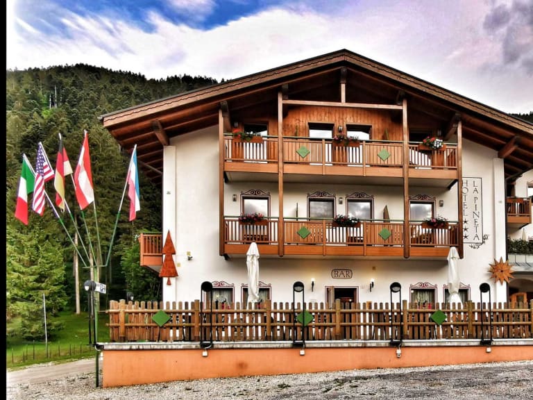 Das Hotel Pizzeria La Pineta zeigt sich als dreistöckiges Alpenhotel mit weißer Fassade und Holzbalkonen in Tiroler Baus