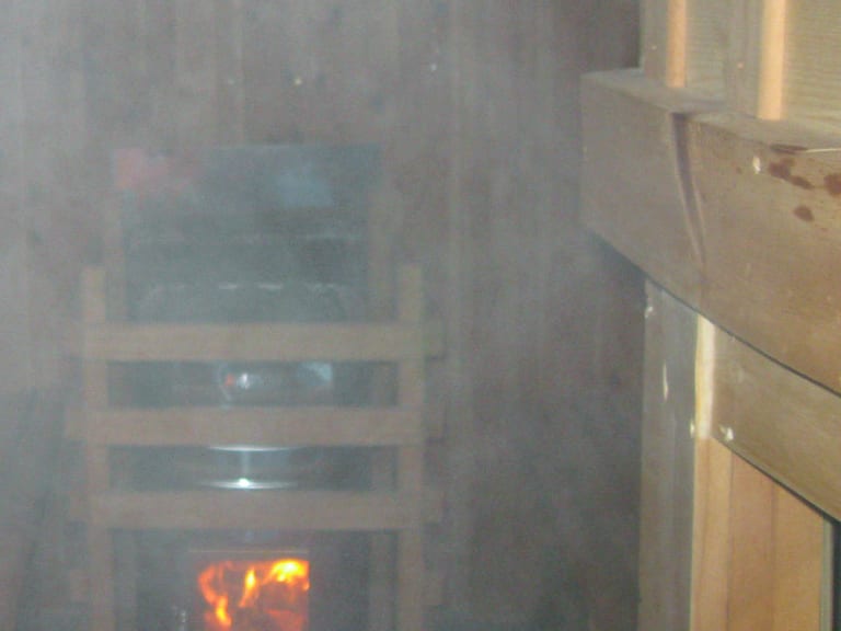 Innenraum der Sauna im Rifugio Lavarella mit gemauertem Holzofen, Dampf und traditioneller Holzausstattung.