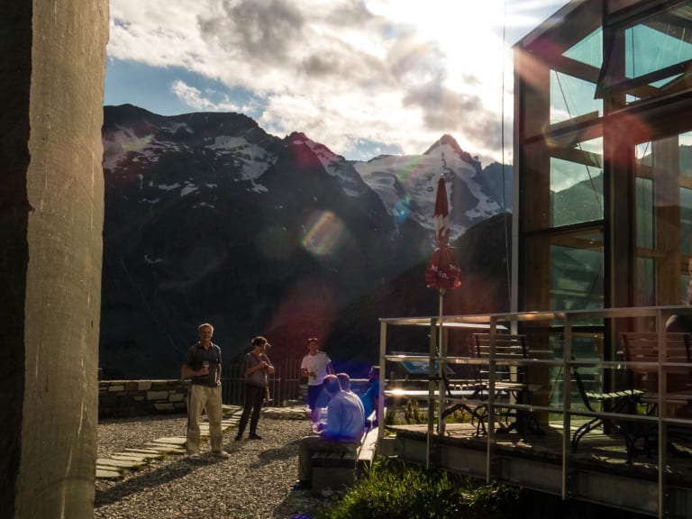 Terrasse von Das Glocknerhaus mit Personen und Ausblick auf die schneebedeckten Berggipfel der Hohen Tauern bei warmer Lichtstimmung.