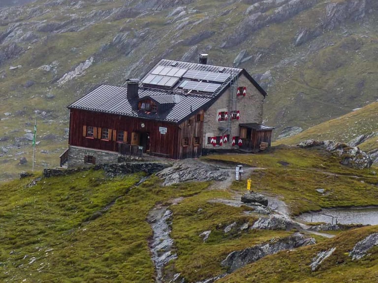 Panoramablick auf die Sudetendeutsche Hütte mit Wellblechdach und Solarpaneelen auf grasbewachsener Hochalm.