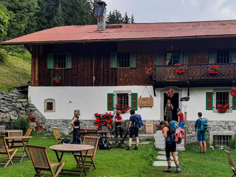 Wandergruppe mit Rucksäcken vor dem Chalet refuge de Nant Borrant, einem zweistöckigen Alpenchalet mit Holzbalkon und Außenterrasse.