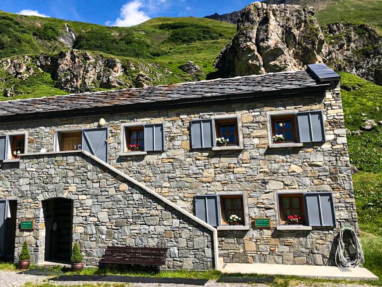 Das Refuge des Mottets mit traditioneller Steinarchitektur und blauen Fensterläden steht auf einer gepflasterten Fläche 