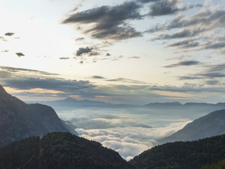 Blick vom Dom na Komni durch ein V-förmiges Tal über eine geschlossene Wolkendecke in den Julischen Alpen.