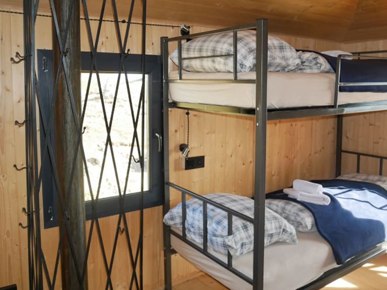 Mehrbettzimmer der Berghütte Meria Keli mit Stockbetten und hellem Holzinterieur auf 2400 m Höhe.