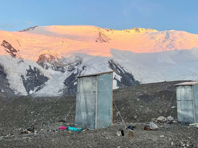 Blaue Toilettenhäuschen im Advanced Base Camp ABC Pik Lenin vor vergletscherter Bergkette im Abendlicht.
