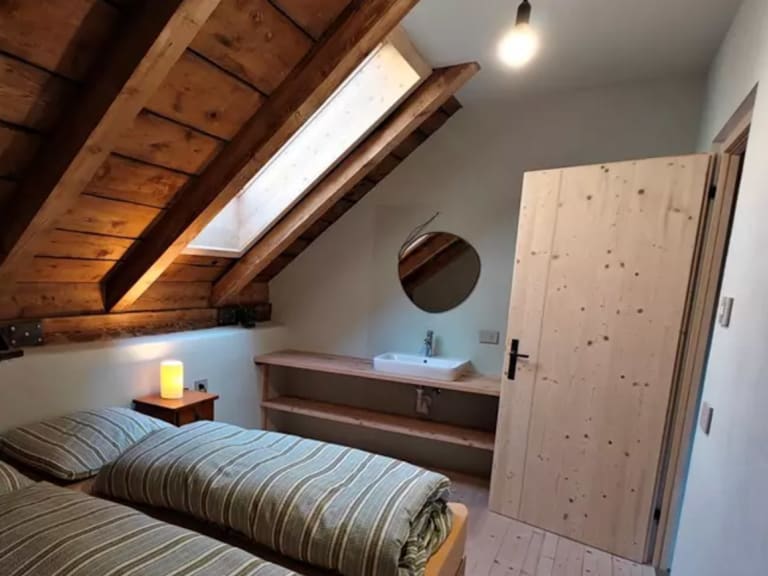 Dachgeschoss-Schlafzimmer der ANAS126 Lodge mit sichtbaren Holzbalken, zwei Einzelbetten und Zirbenholz-Kleiderschrank.
