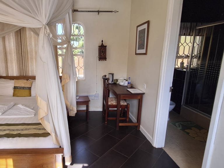 Doppelzimmer im Entebbe Palm Hotel mit Himmelbett, weißem Moskitonetz und tropischem Ausblick durch Sprossenfenster.