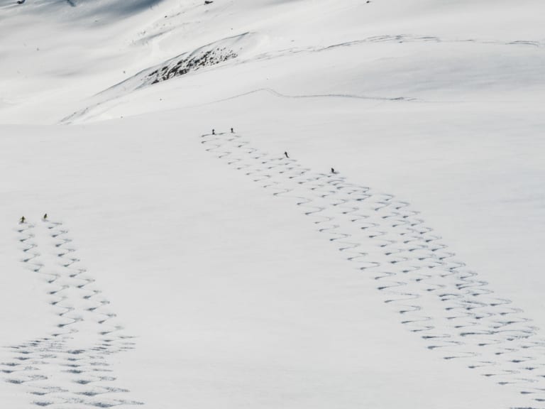 Sechs Skitourengeher fahren in zwei Gruppen durch Pulverschnee an einem weitlaeufigen Hang in den Lyngen Alps ab.
