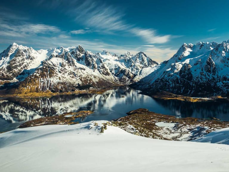 Skitour auf den Lofoten: verschneiter Hang mit Blick auf Fjord und Bergkette im Winter.
