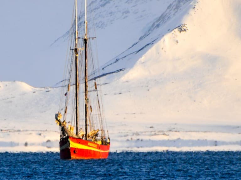Skitour auf Svalbard: Segelschiff vor schneebedecktem Berghang in Spitzbergen im Winter.