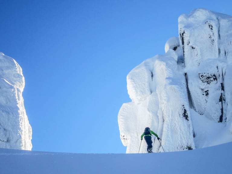 Bergführer Sebastian Conrad fährt mit Tourenskiern durch pulvrigen Tiefschnee zwischen weiß verhangenen Felsformationen.