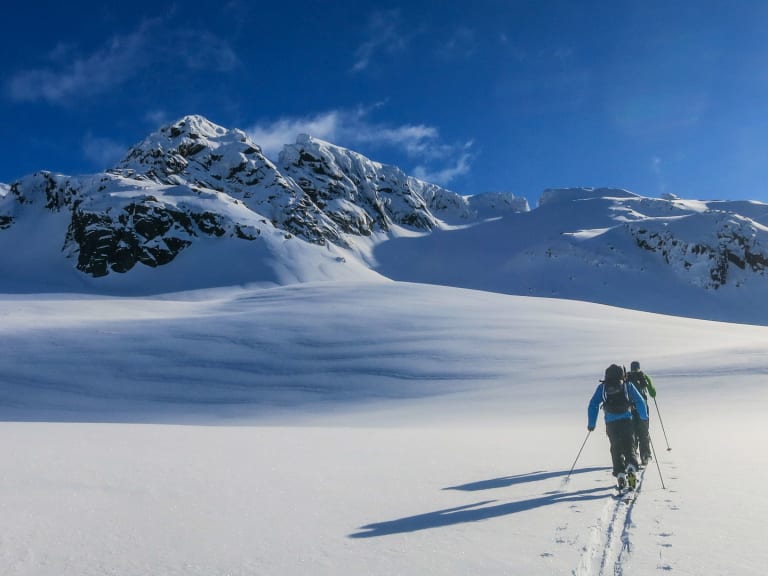 Zwei Skitourengeher bewegen sich durch unberührten Tiefschnee, geführt von Bergführer Sebastian Conrad in blauer Jacke.