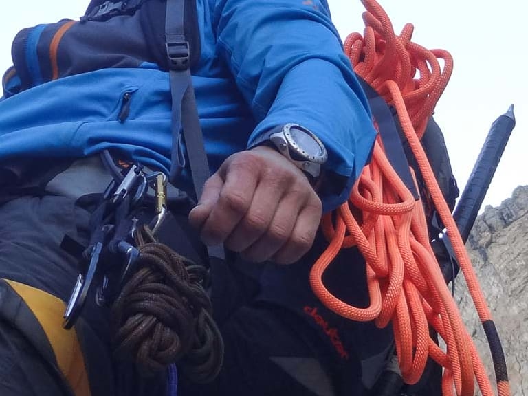 Bergführer Jens Lang in blauer Softshelljacke mit orangefarbenem Kletterseil vor steilen Kalksteinfelsen.