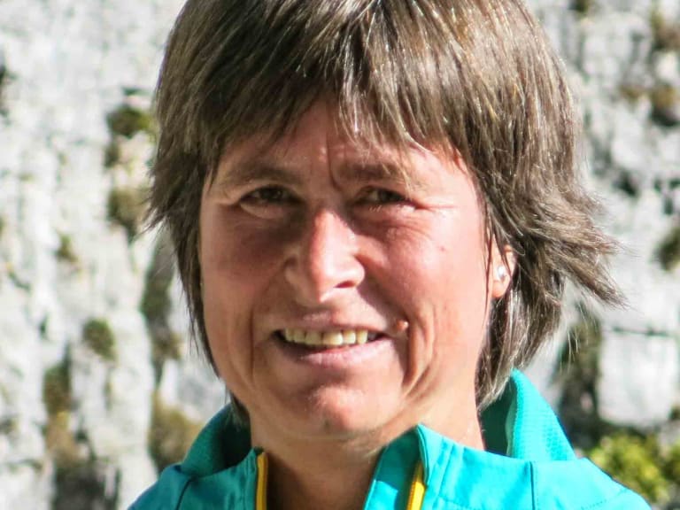 Portrait von Bergwanderführerin Angelika Neubauer mit türkiser Jacke vor einer strukturierten Kalksteinwand bei Tageslicht.