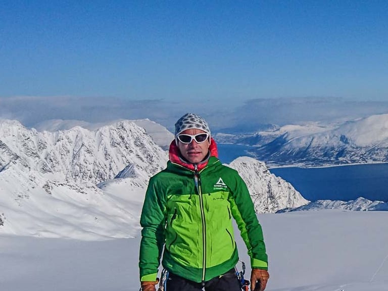 Bergführer Jörg Rauschenberger steht auf dem verschneiten Tafeltinden vor weitläufiger Fjordlandschaft in den Lyngen Alpen.