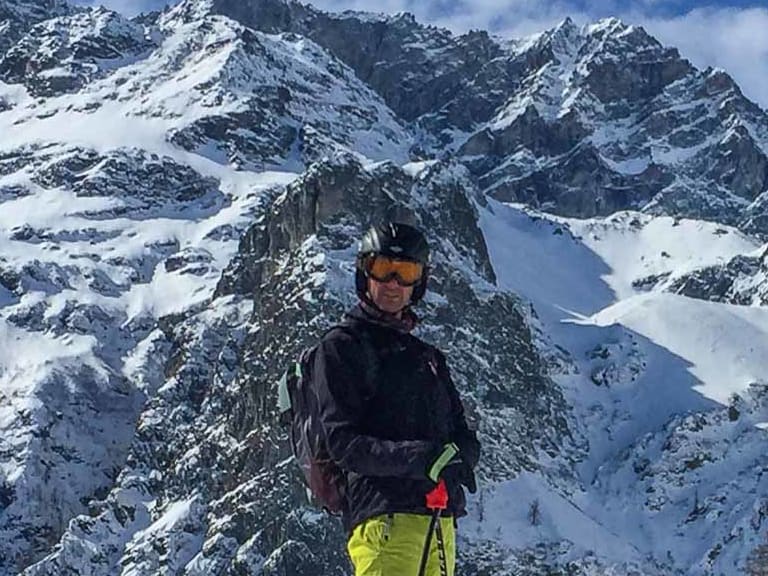 Bergwanderführer Karlheinz Rösch auf Skiern in verschneiter Landschaft mit Bergdorf und Gipfeln im Hintergrund.