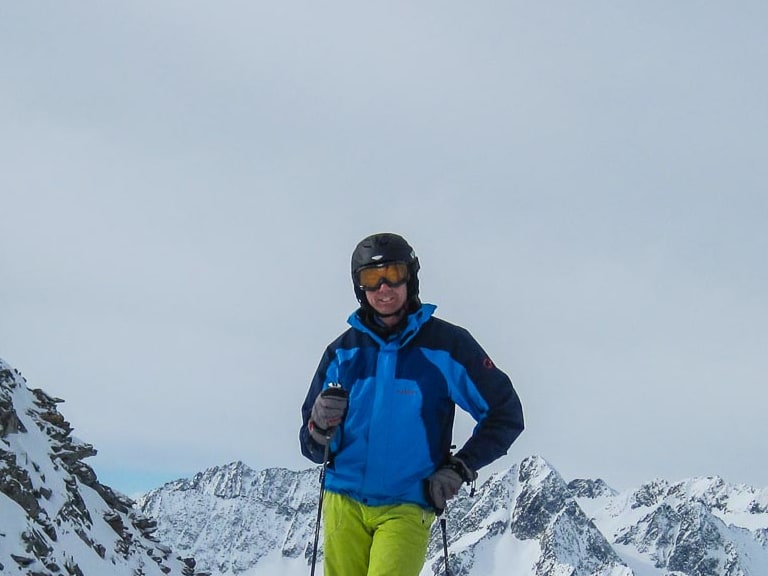 Auf einem verschneiten Berggipfel steht Bergwanderführer Karlheinz Rösch mit Skistöcken vor Bergpanorama.