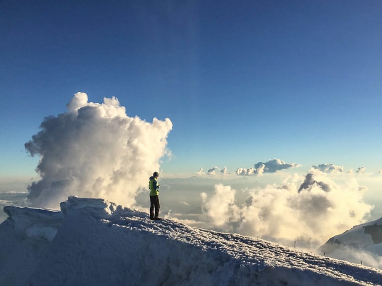 Bergführer Michael Rüter steht in grüner Jacke auf einem verschneiten Gipfelgrat oberhalb der Wolken.