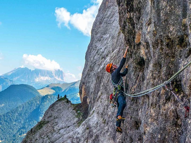 Bergführer Michael Rüter klettert mit orangem Helm an einer steilen Felswand entlang eines Drahtseils.