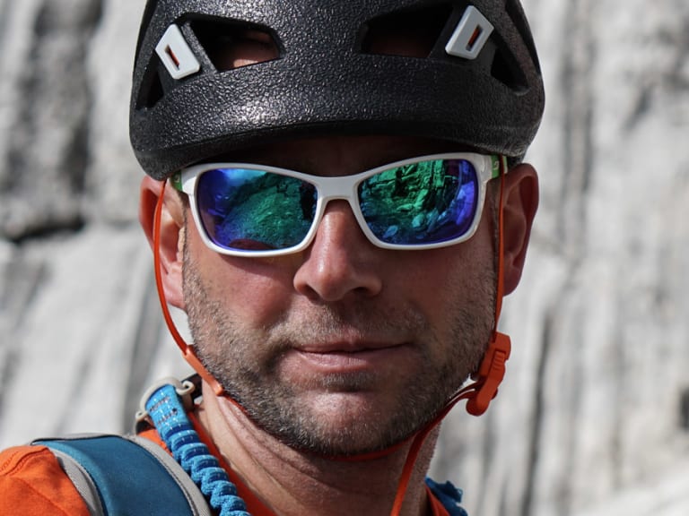 Guide Markus Schubert trägt schwarzen Petzl-Kletterhelm mit weißer Sonnenbrille und hält blaues geflochtenes Seil am Gurt.