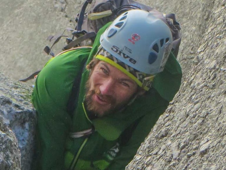 Beim Klettern an grau-beigem Fels greift Bergführer Philipp Berg aktiv in eine Felsritze und lächelt in die Kamera.