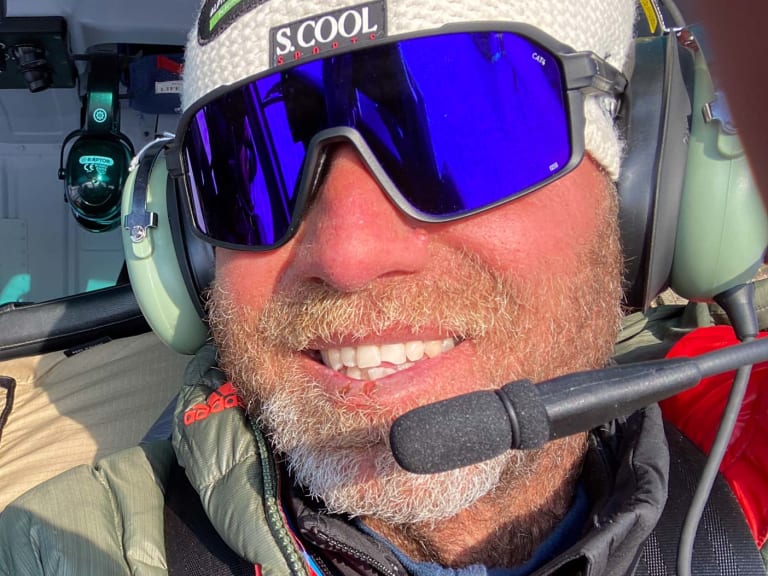 Bergführer Christian Knabe sitzt im Hubschrauber mit Headset und blonder Skibrille, dahinter eine zweite Person mit Sonnenbrille.