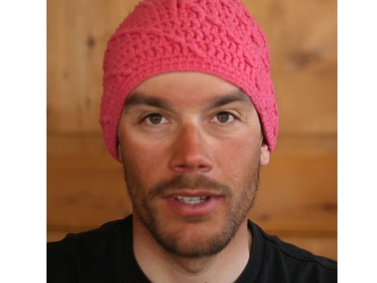 Bergführer Philipp Neumann trägt eine rosa gestrickte Wollmütze und schwarzes Shirt in einem Innenraum mit Holzwand.