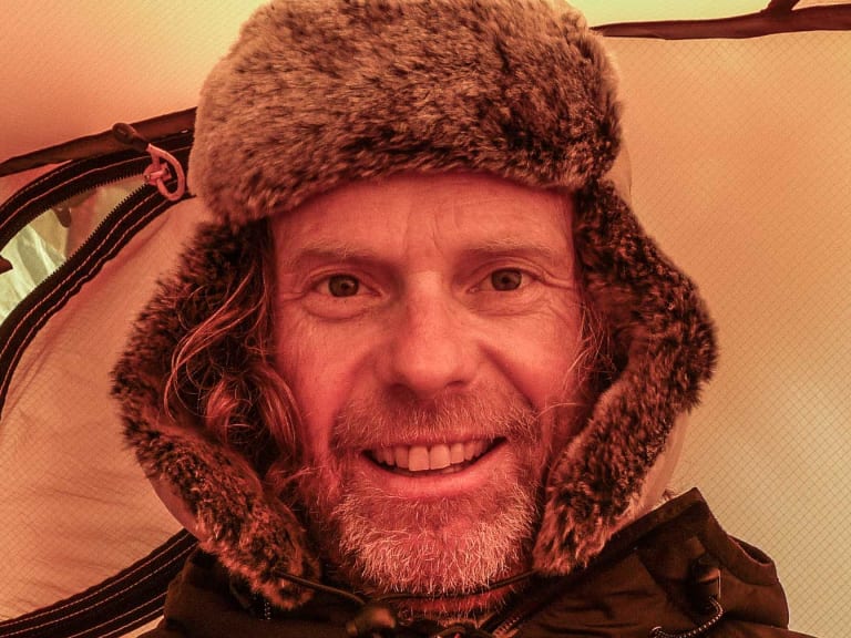 Bergführer Andreas Bucher trägt eine braune Fellmütze mit Ohrenklappen und lächelt in warmer Innenraumbeleuchtung.