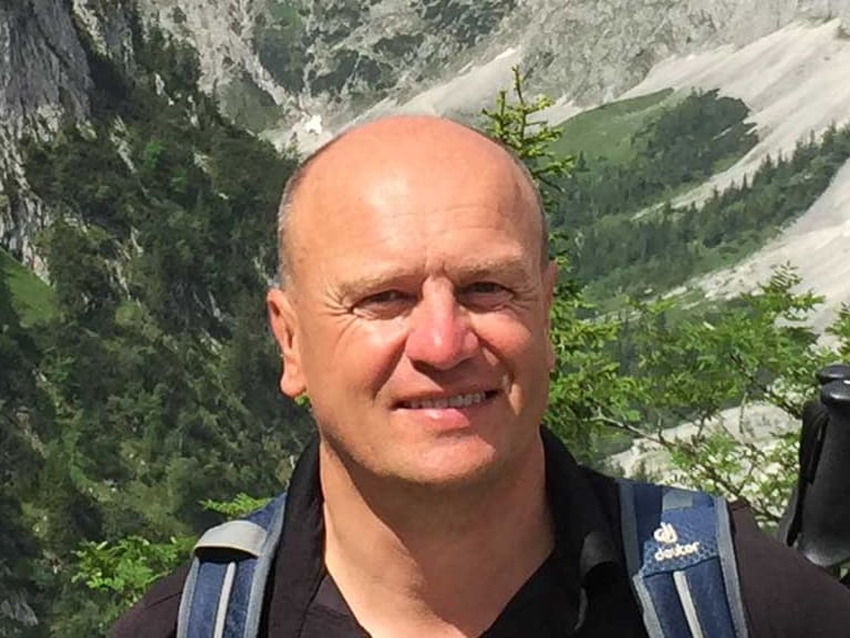 Mit schwarzem Poloshirt und blauem Wanderrucksack steht Bergwanderführer Peter Kohl vor einem tiefen Tal mit steilen Kalksteinwänden.
