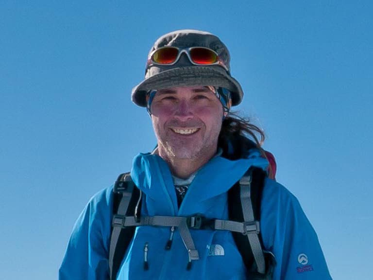 Bergwanderführer Markus Arndt in blauer Winterjacke und grauem Sonnenhut vor schneebedeckten Gipfeln.