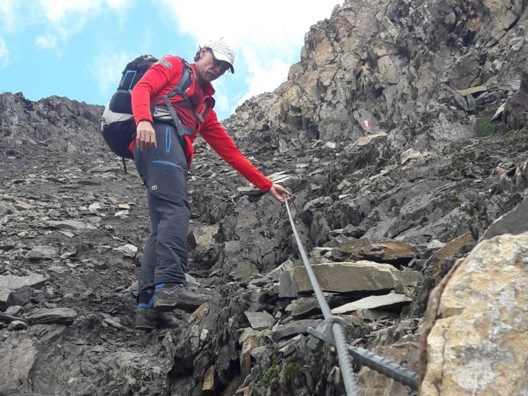 Über Geröll und Felsbrocken steigt Bergwanderführer Thomas Schill in roter Jacke durch eine Kalksteinrinne.